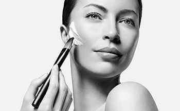 A woman is applying cream to her face with a brush.