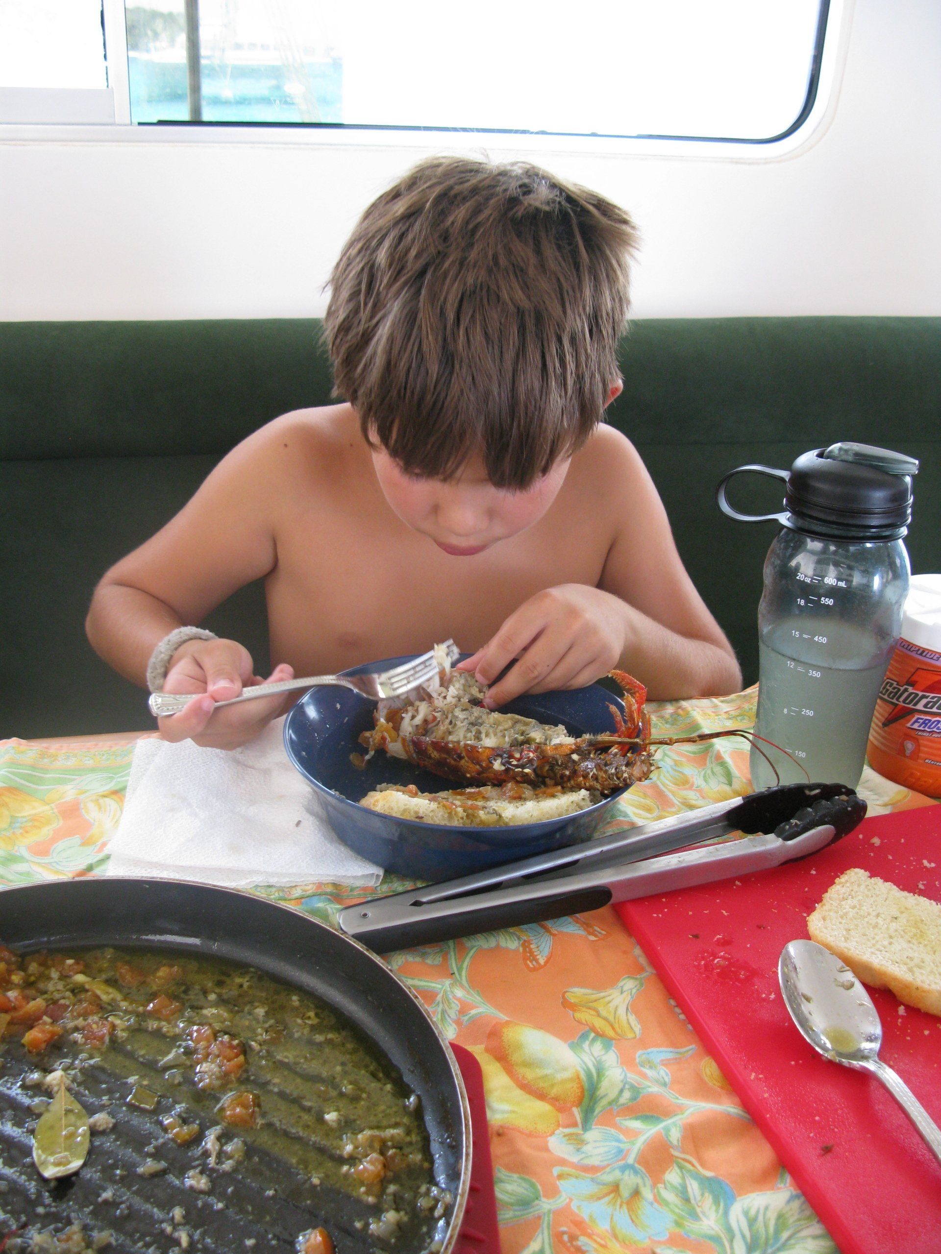 A shirtless boy is eating from a bowl on a table