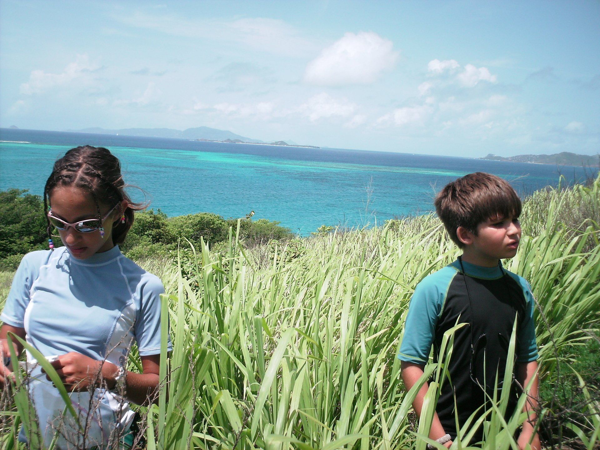 A boy and a girl are standing in a field with the ocean in the background