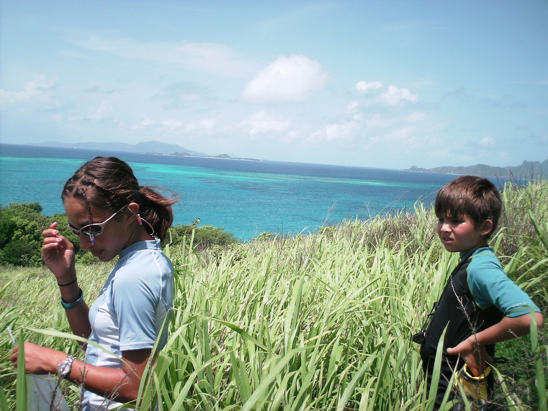 A boy and a girl are standing in a field with the ocean in the background