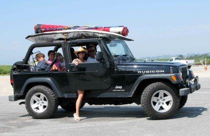 A black jeep with a surfboard on top of it