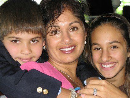 A woman is holding two children and smiling for the camera
