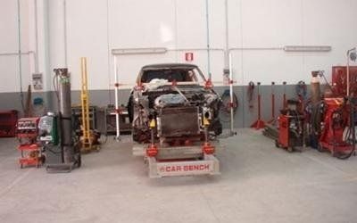 Officina meccanica con un'auto smontata su un banco di lavoro con struttura rossa e attrezzi tutt'intorno.
