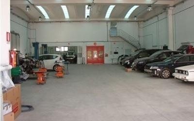 Ampia officina meccanica con auto parcheggiate lungo la parete destra e attrezzi sulla sinistra.