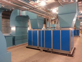 Industrial HVAC units and blue ductwork in a mechanical room with exposed ceiling pipes