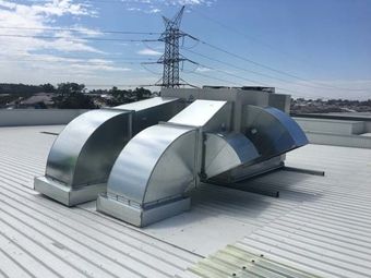 Rooftop metal ventilation ducts on a white industrial roof under a blue sky, with power lines in the background