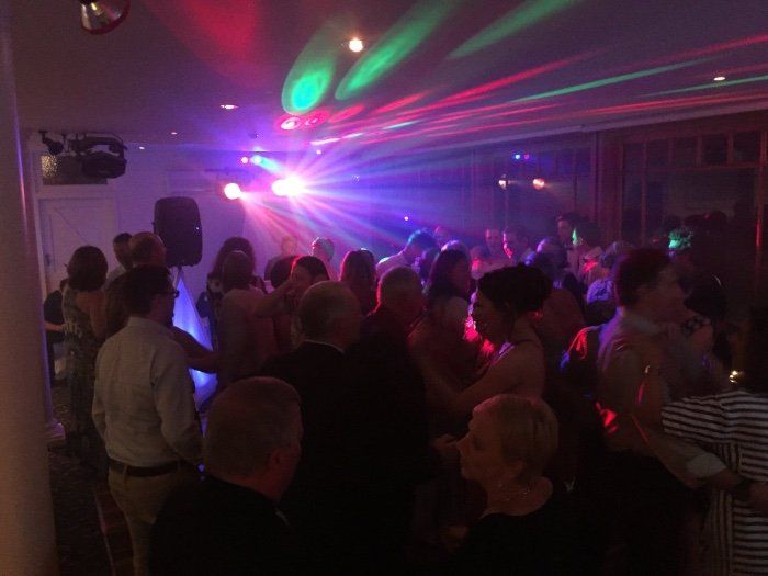 A large group of people are dancing in a room with lots of lights.