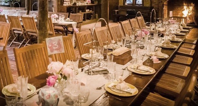 A long table with plates , glasses , and flowers on it in a restaurant.