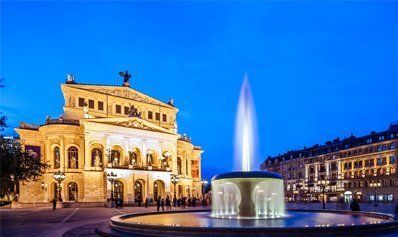 A fountain in front of a large building at night.