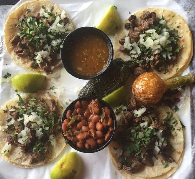 Four tacos, salsa, beans, peppers, lime wedges. Overhead shot.