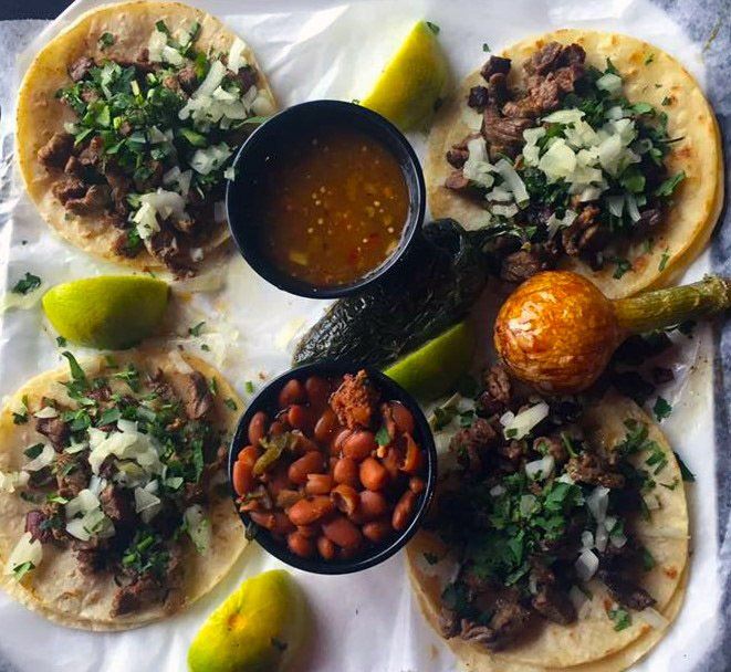 Tacos with meat, cilantro, and onion, served with salsa, beans, limes, and roasted peppers.