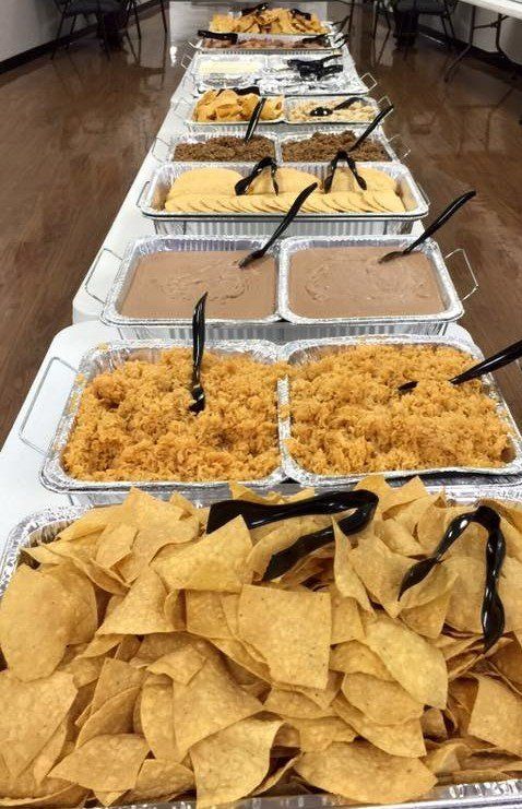 Long table with various Mexican food trays: chips, rice, beans, and other dishes.