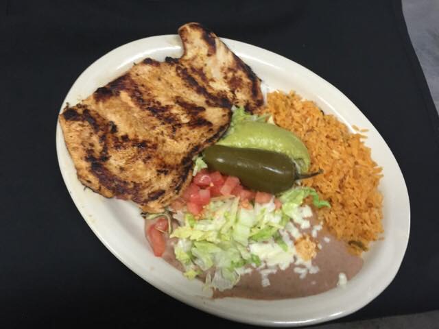 Grilled chicken breast, rice, beans, lettuce, tomato, jalapeno, and avocado on a plate.
