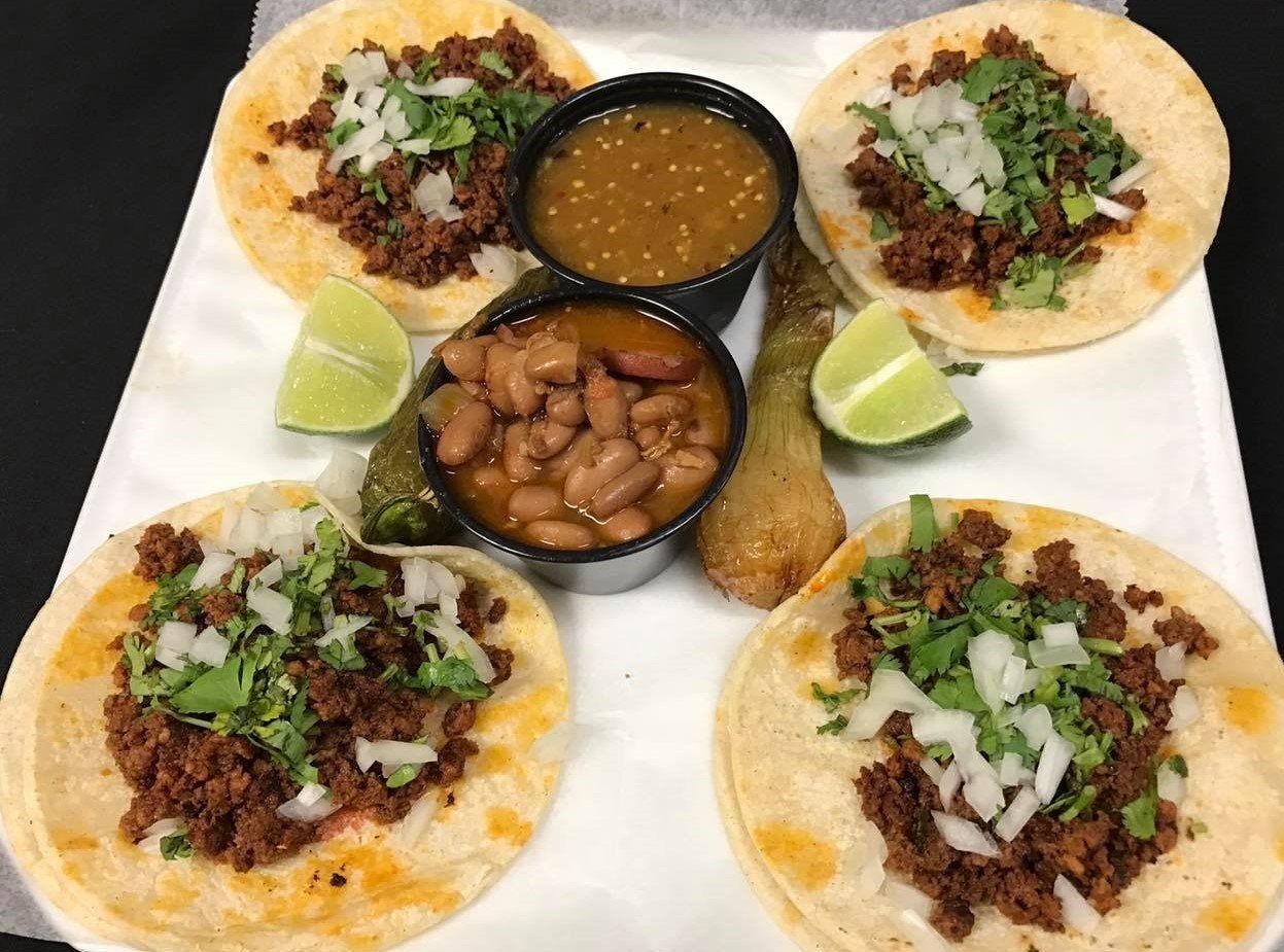 Tacos with meat, onion, cilantro, lime wedges, salsa, and beans on a white plate.