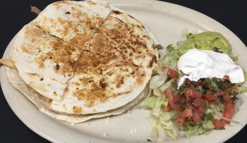 Quesadilla with side of guacamole, sour cream, and salsa on a plate.