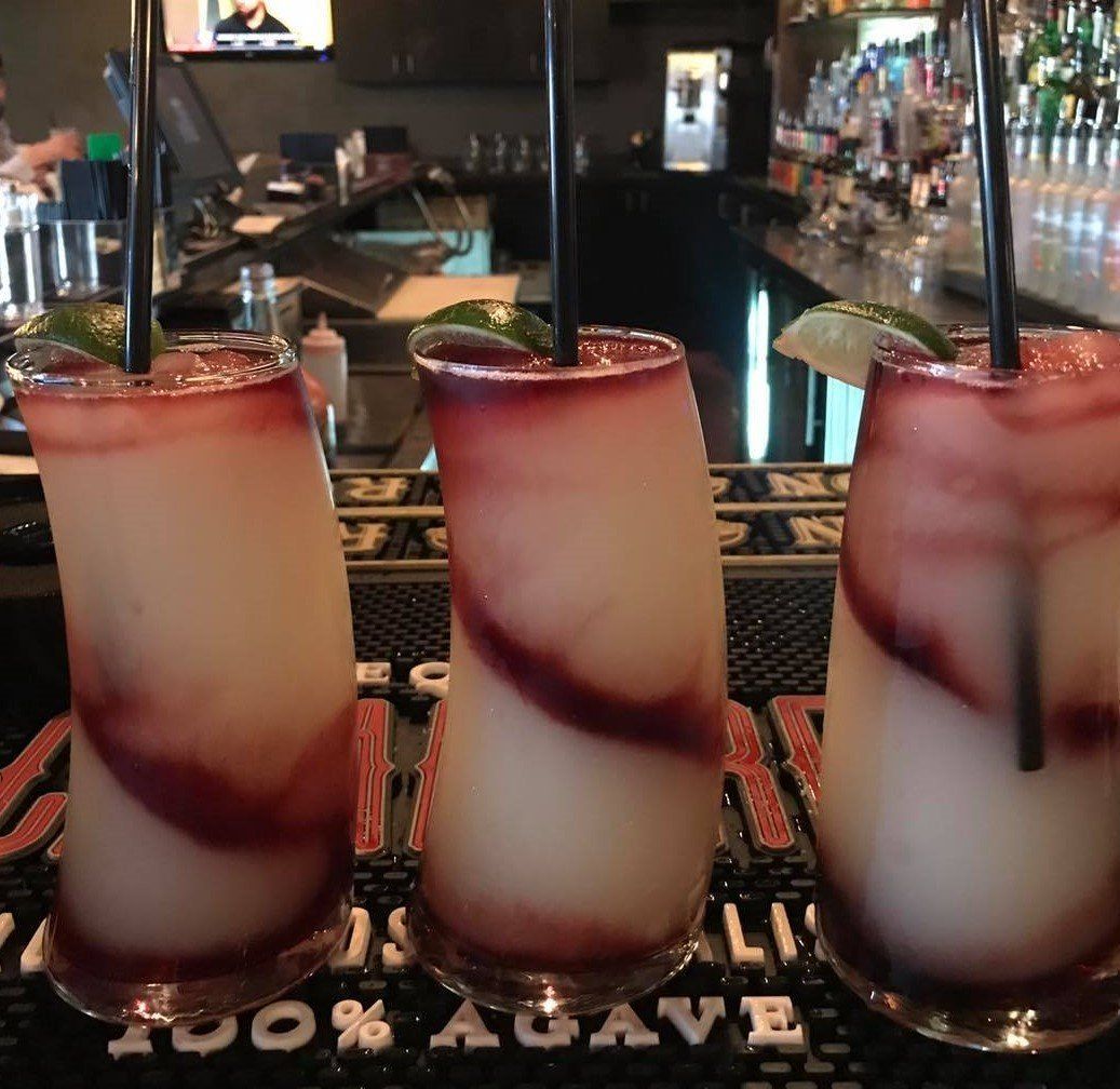 Three layered cocktails with black straws and lime garnishes on a bar.