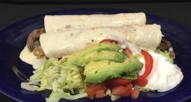 Enchiladas with avocado, tomato, lettuce, and sour cream on a blue plate.