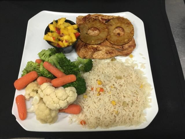Chicken, rice, and vegetables served with mango salsa and pineapple slices.