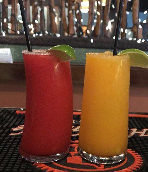 Two frozen cocktails, one red and one yellow, with straws and lime wedges, on a bar.