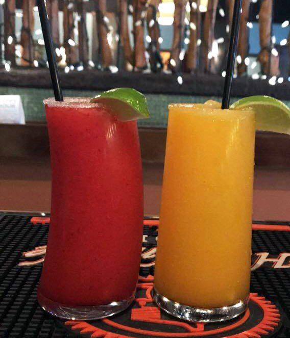 Two colorful, frosty cocktails with lime wedges and straws, on a bar. One is red, the other is orange.