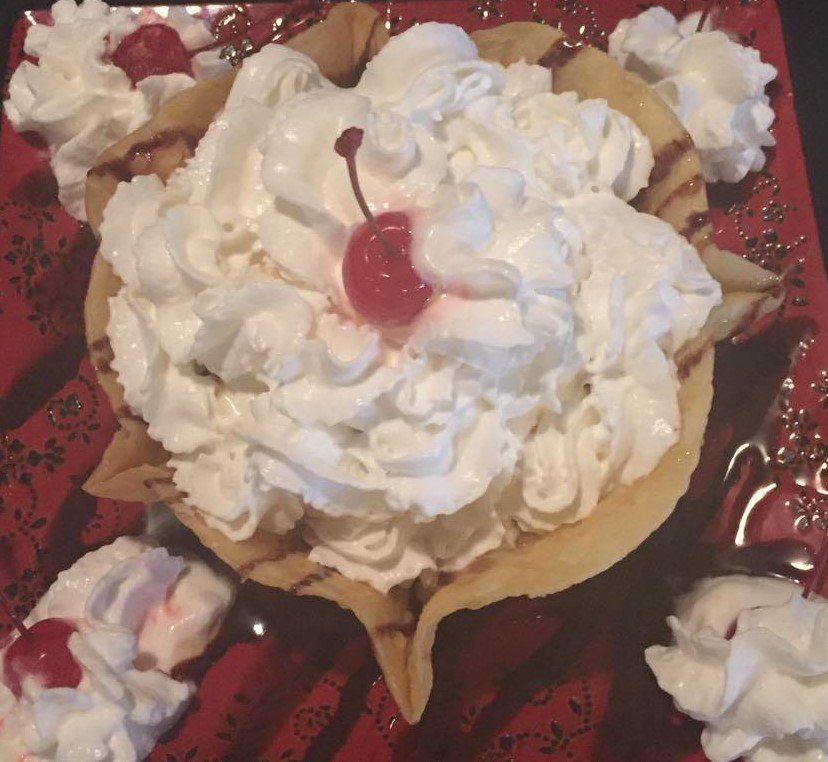 Dessert in a fried tortilla bowl, filled with whipped cream and a cherry, served on a red plate.