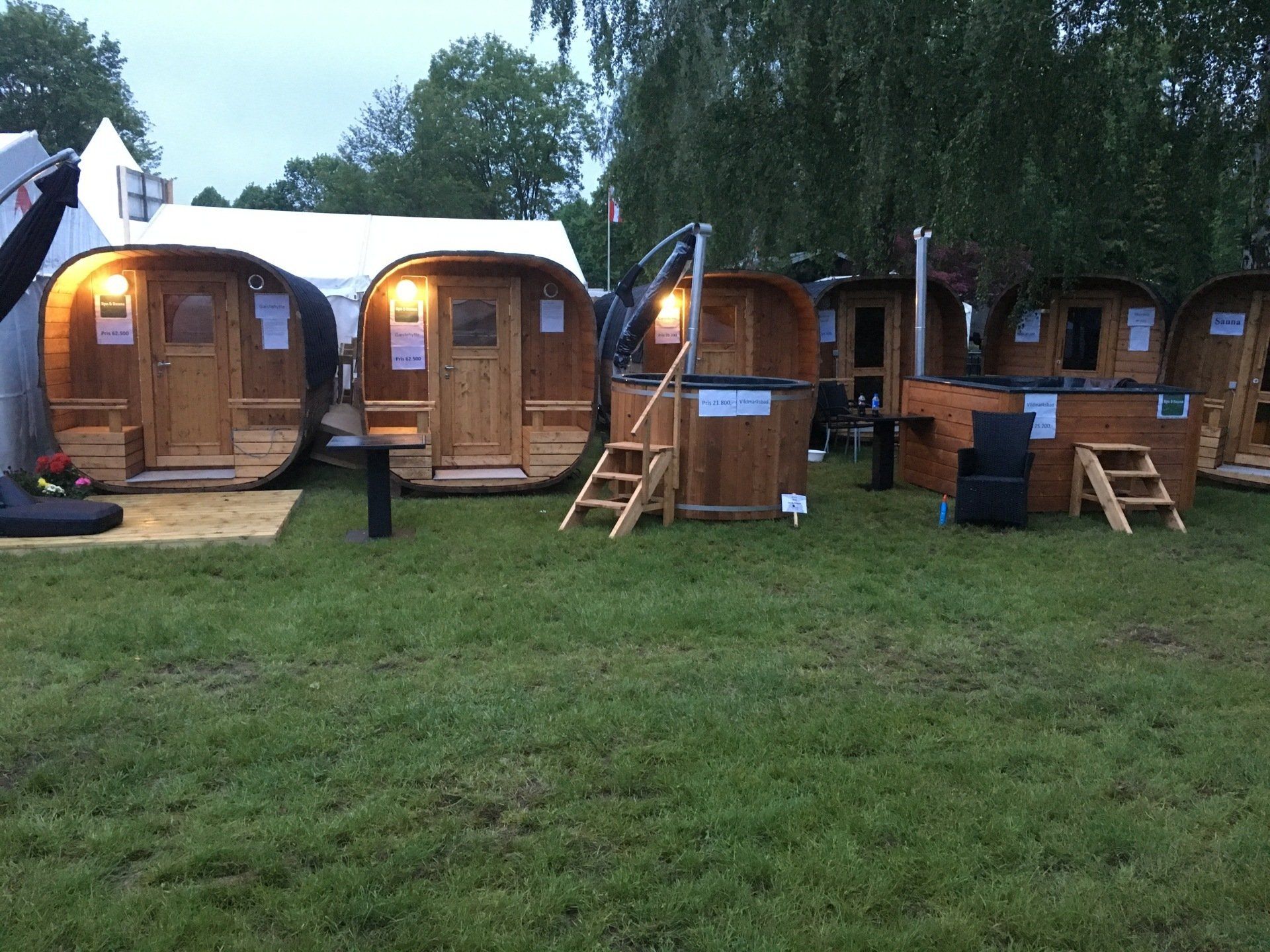 Række af små træhytter på en græsklædt campingplads i skumringen, med trapper og lys, der lyser indenfor.