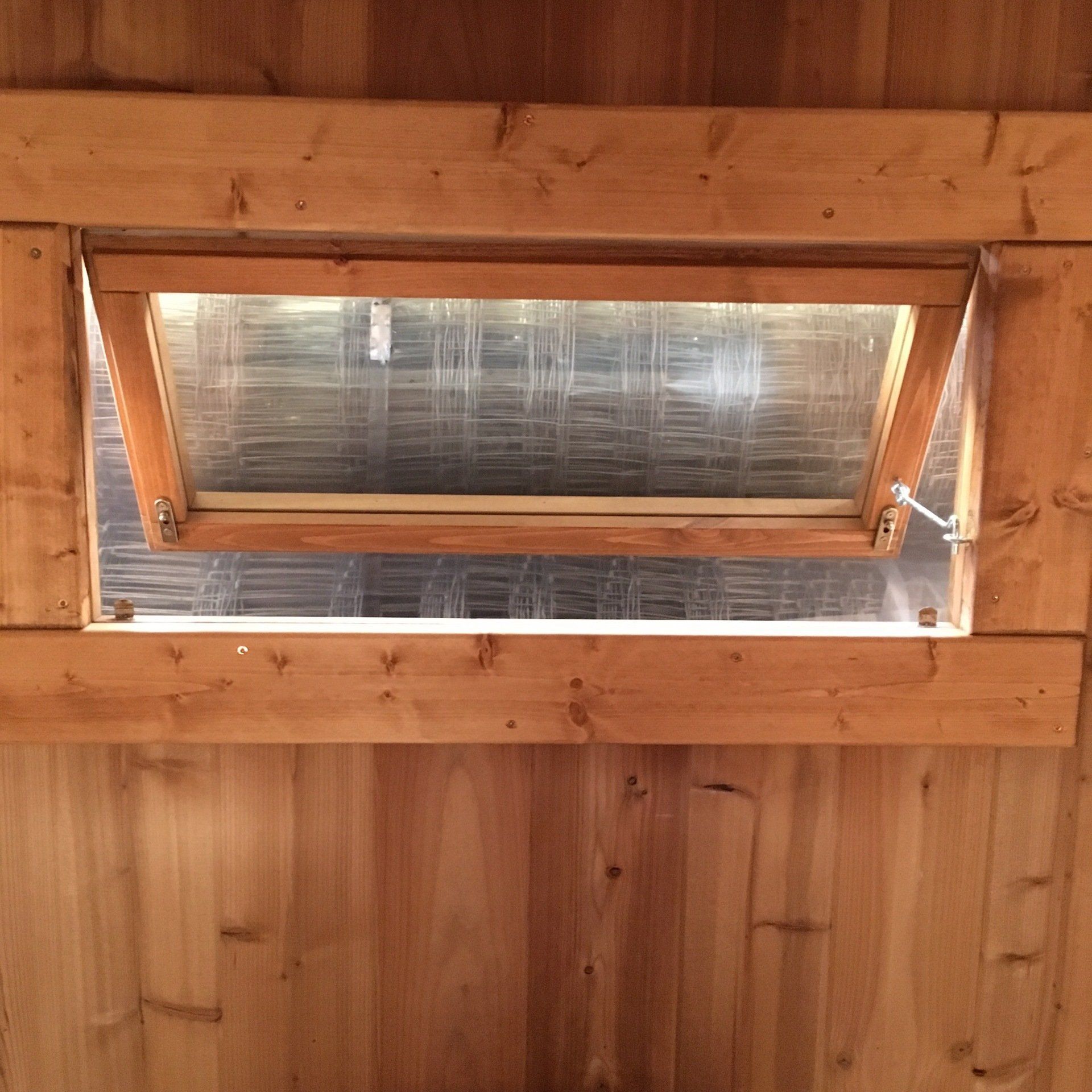 Træpanelvæg med et lille åbent ovenlysvindue eller ventilationsåbning, der lukker dagslyset ind