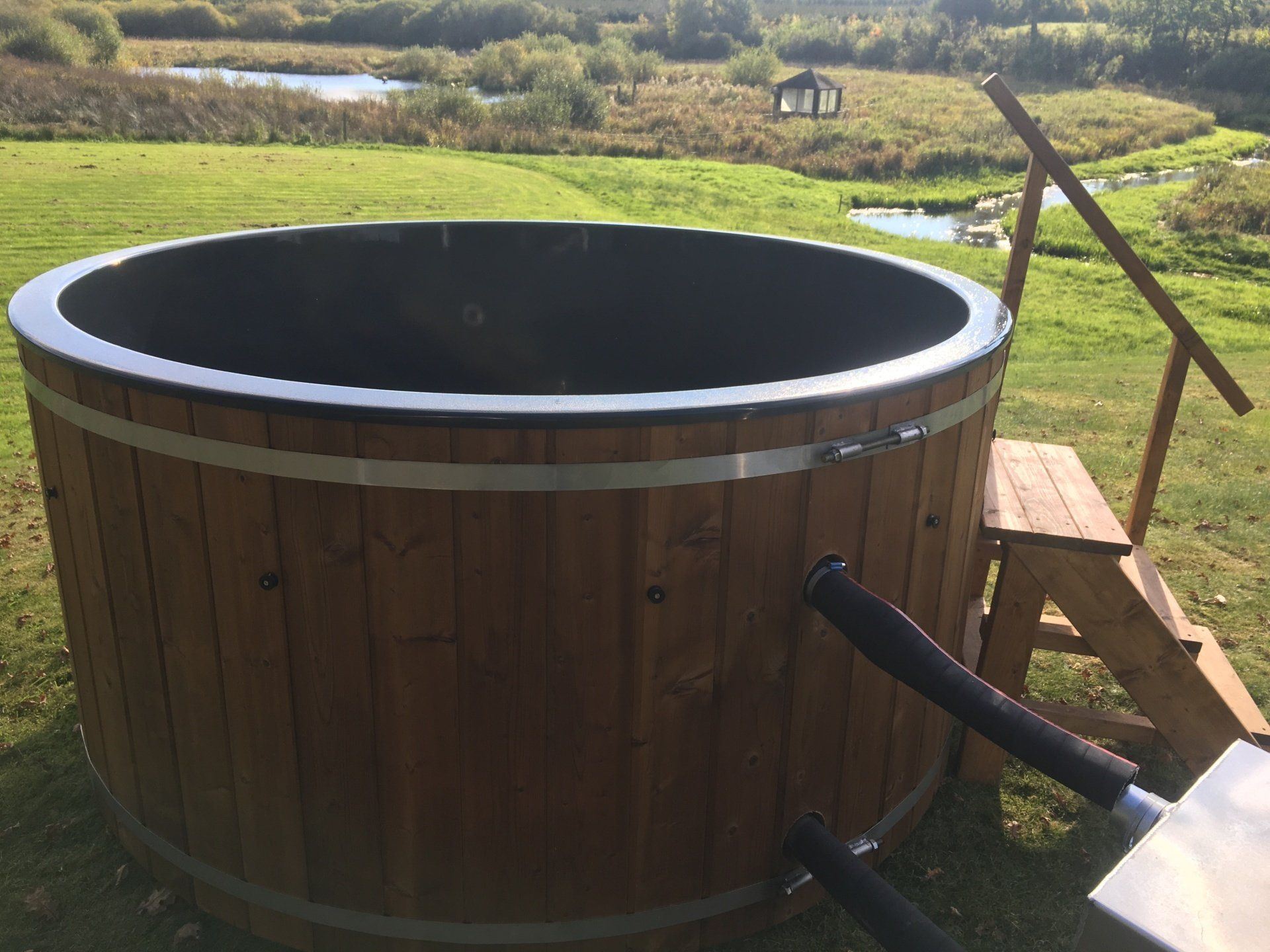 Udendørs træjacuzzi på en græsklædt terrasse med en sort kant og trin i nærheden.