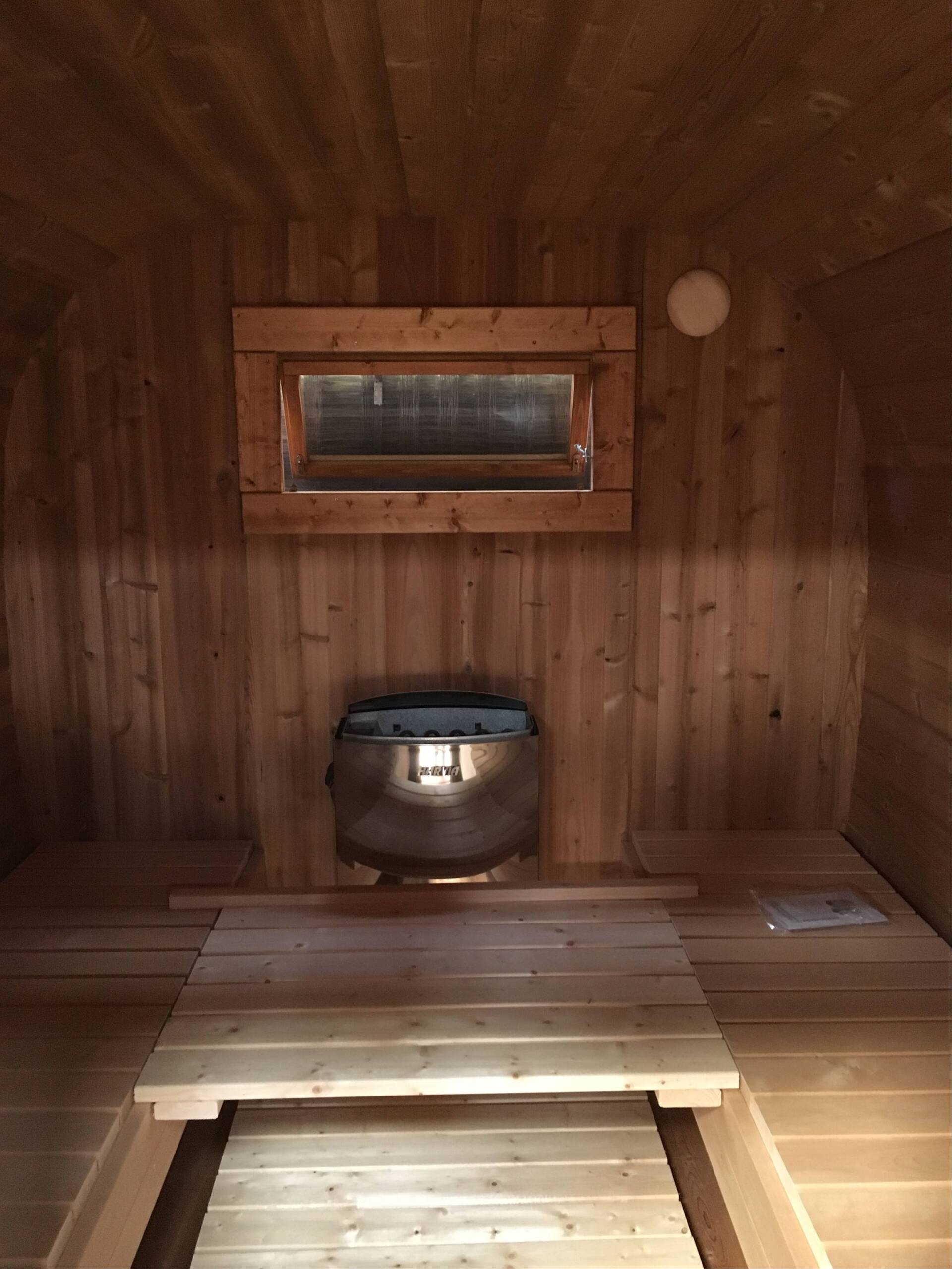 Træsauna med varmeovn og siddepladser indeni.