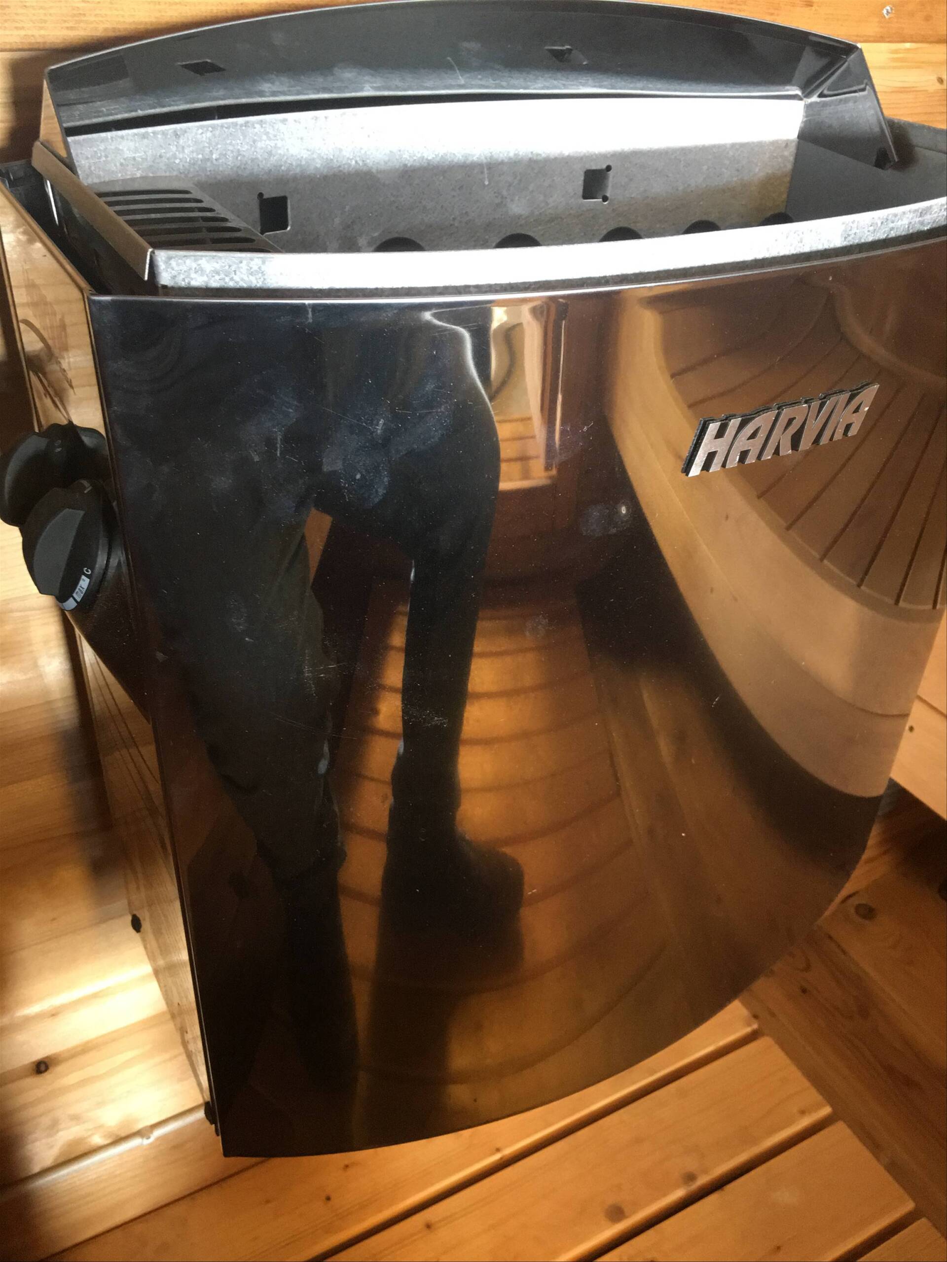 Bærbar forkromet varmelegeme med sort sidepanel på et trægulv, der viser den øverste åbning og mærkemærke