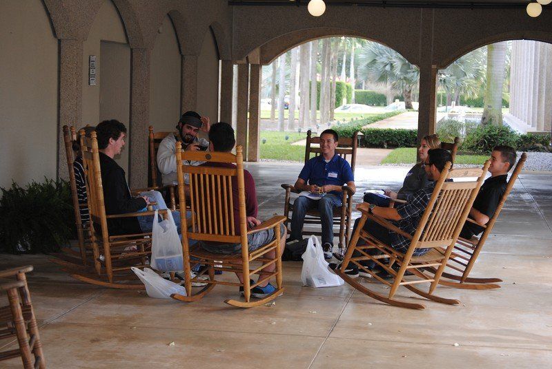 A group sitting on a patio in rocking chairs.
