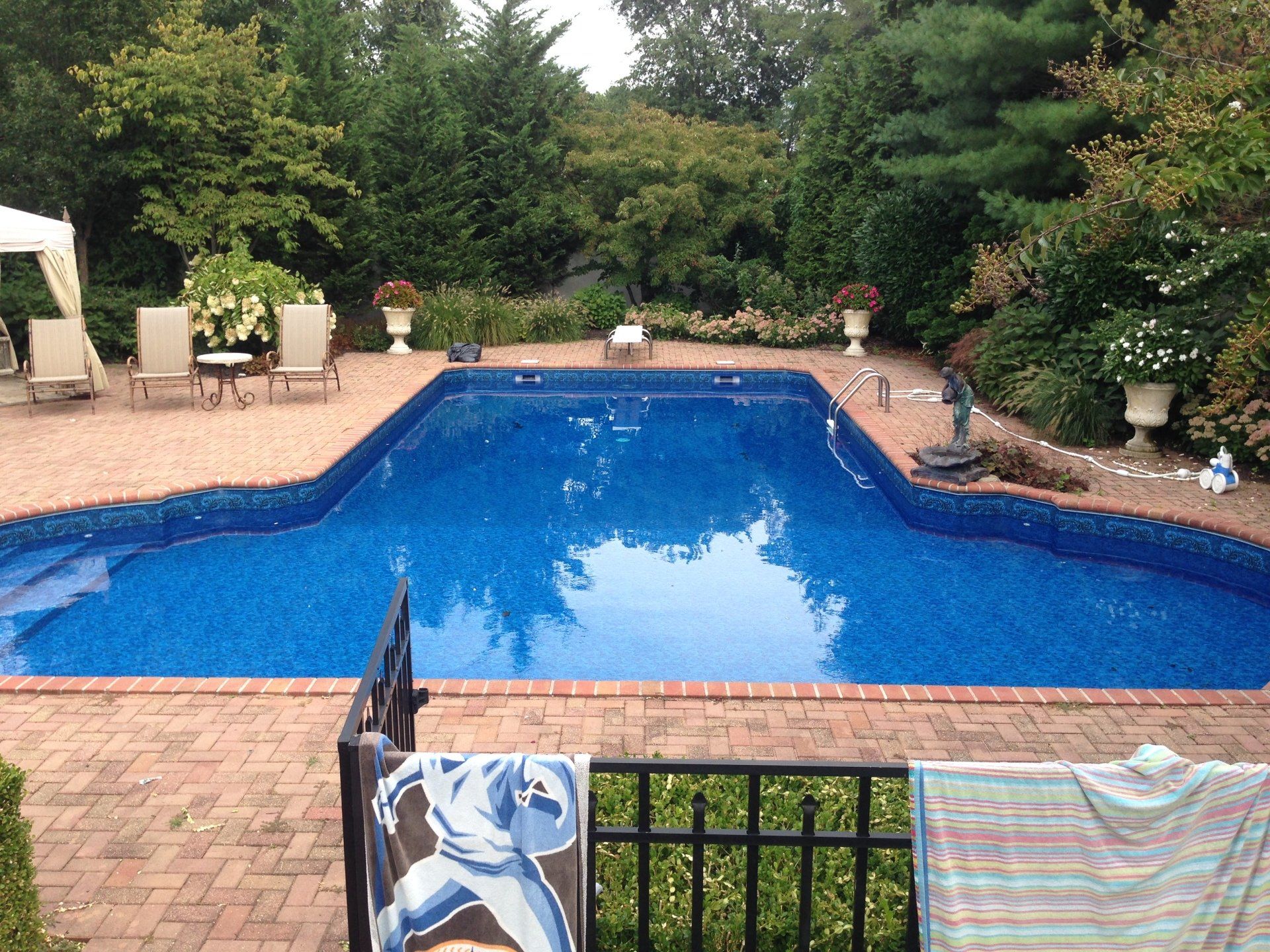 a large swimming pool is surrounded by a brick patio and chairs