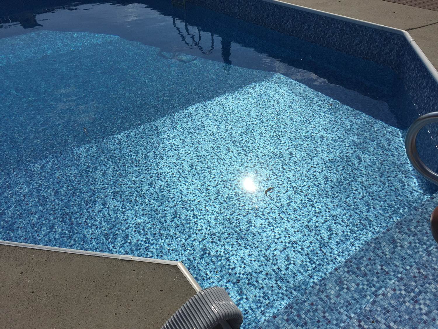 a swimming pool with blue tiles and the sun shining on it