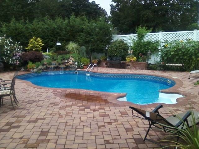 a large swimming pool is surrounded by a brick patio and chairs