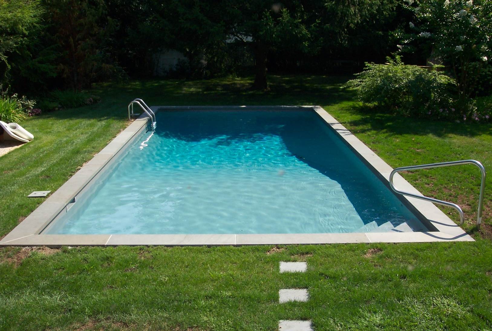 a large rectangular swimming pool surrounded by grass and trees