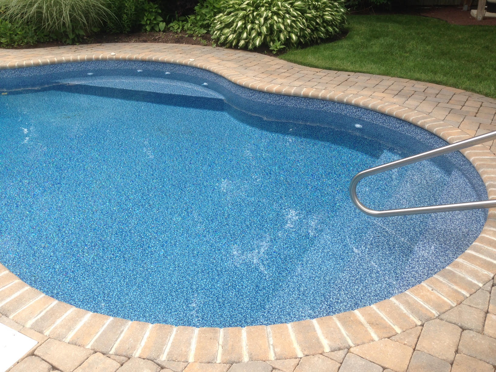a swimming pool with a brick walkway surrounding it