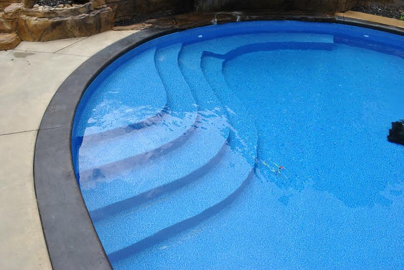 a swimming pool with blue steps and a waterfall in the background