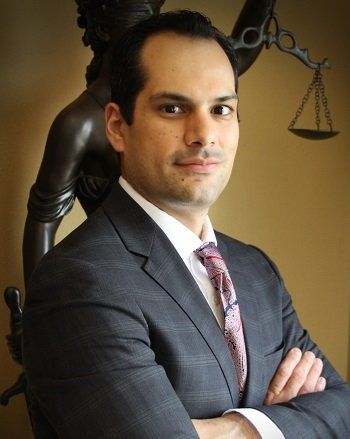 Man in suit, arms crossed, smiling, with statue of Lady Justice in the background.