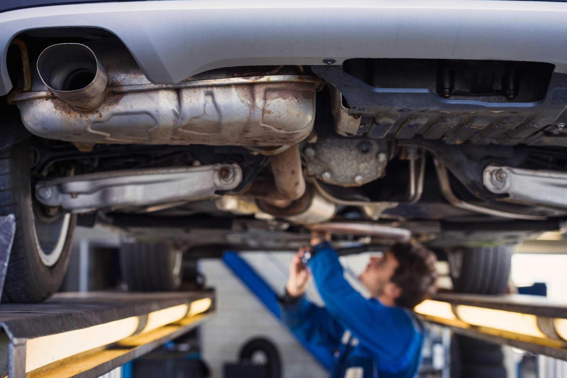 A man is working on the underside of a car in a garage.