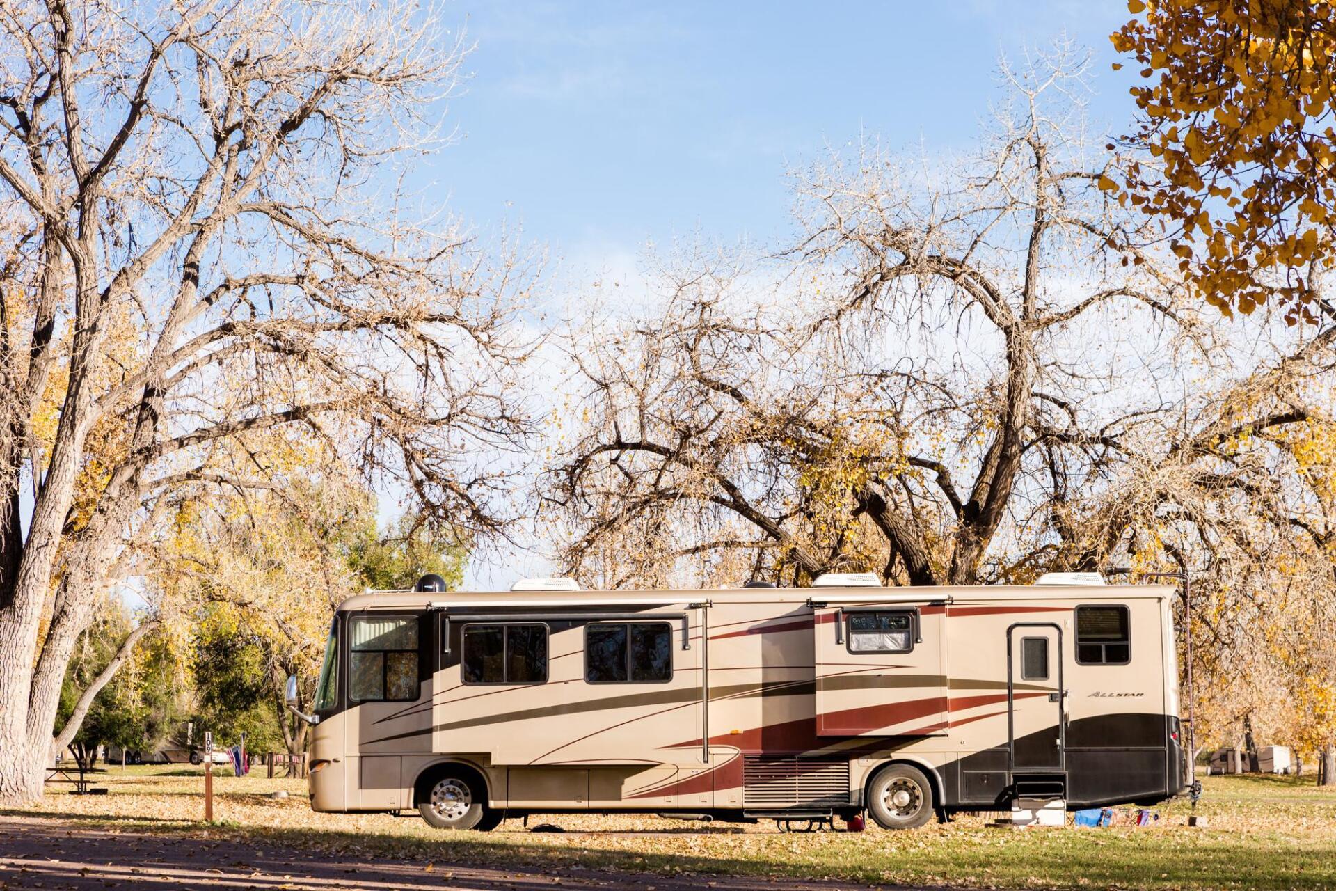 A large rv is parked in a park surrounded by trees.