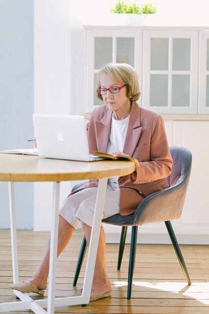 An older woman is sitting at a table using a laptop computer.