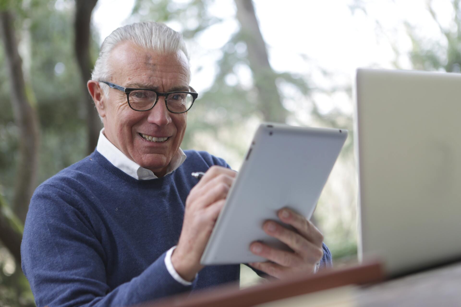 An older man is using a tablet computer in front of a laptop computer.