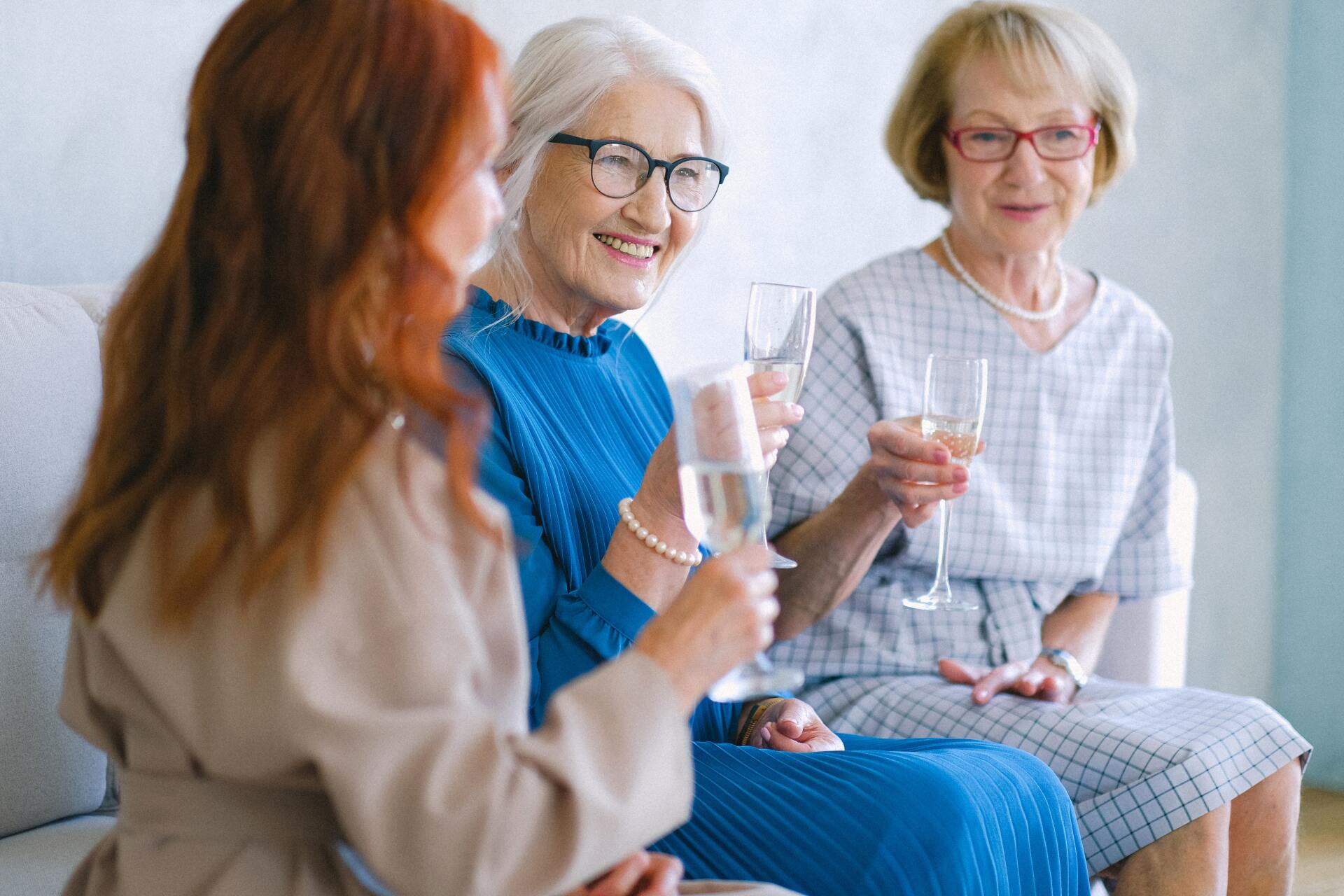 Three women are sitting on a couch holding wine glasses.
