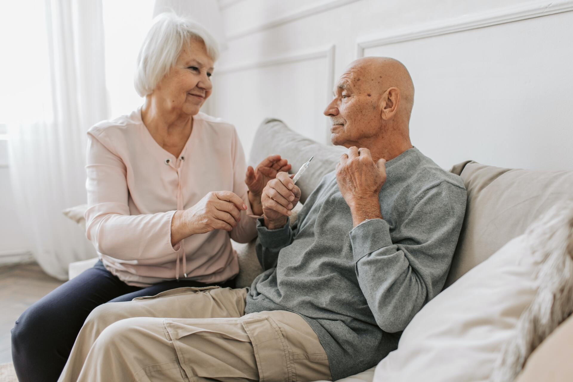 An elderly couple is sitting on a couch and talking to each other.