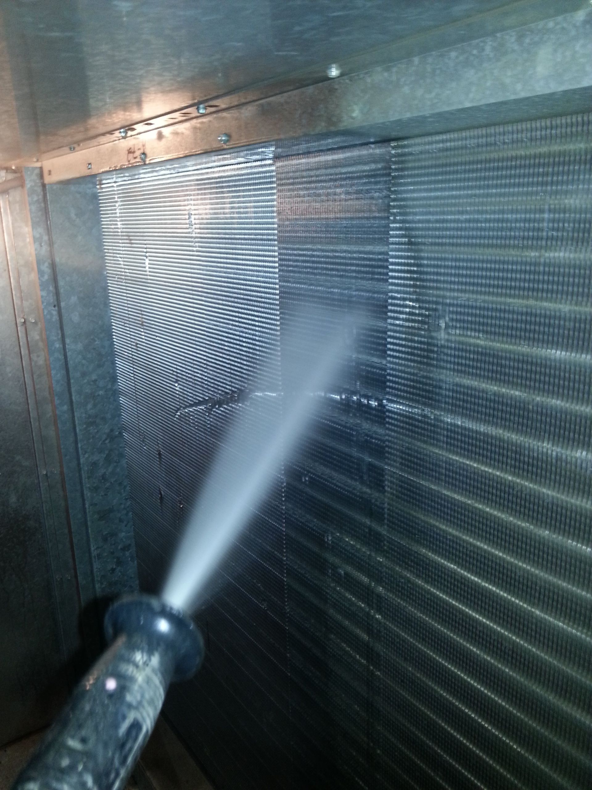 a person is cleaning an aircon condenser with a high pressure washer .