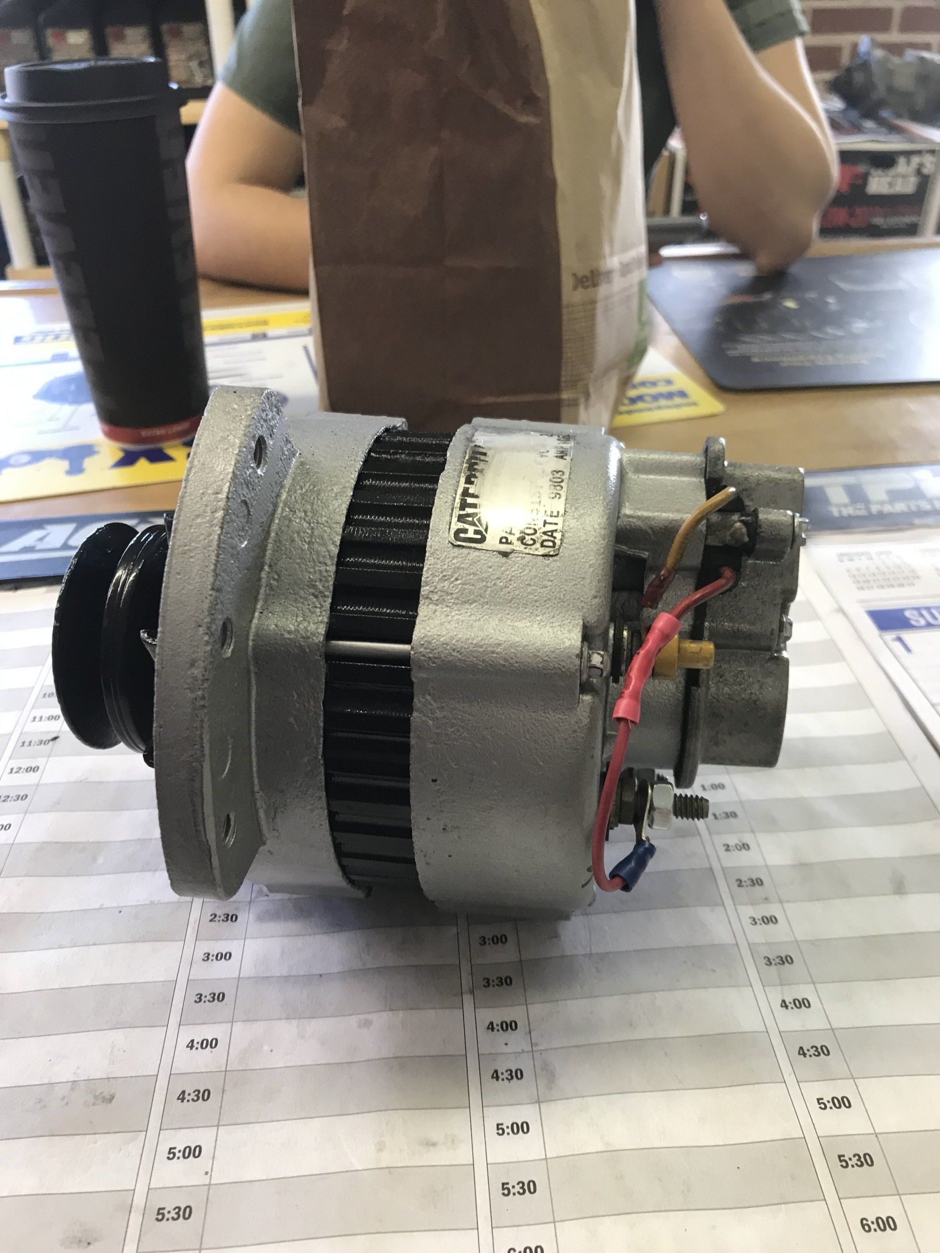Small metallic motor or generator on a tabletop, with exposed wiring and a black front fan assembly.