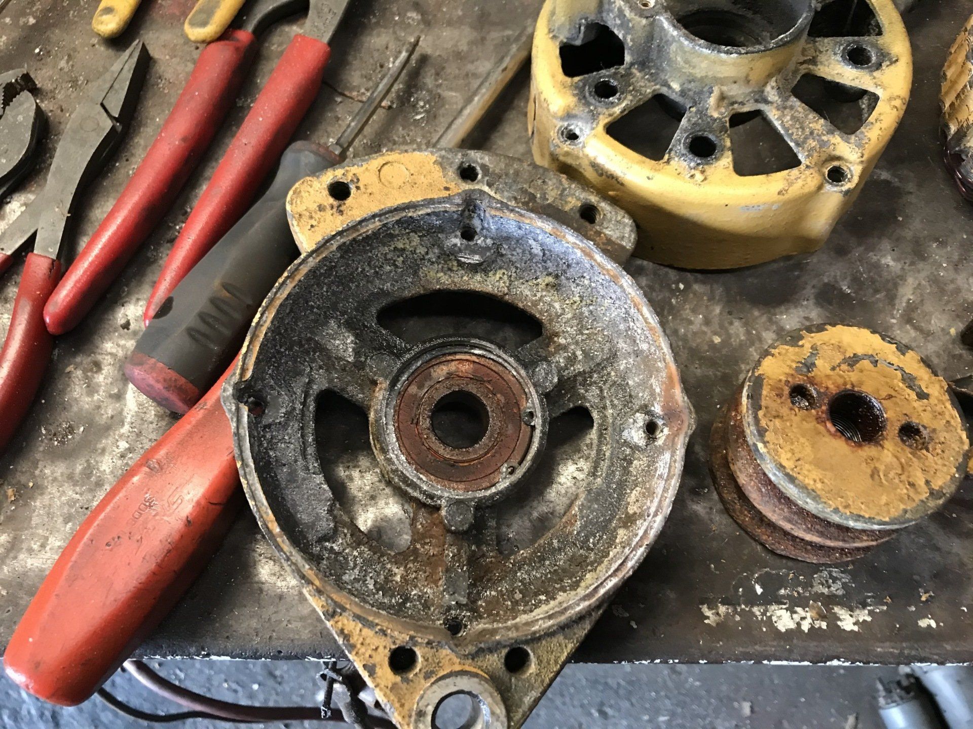 Dirty disassembled metal motor parts and red-handled tools on a workbench