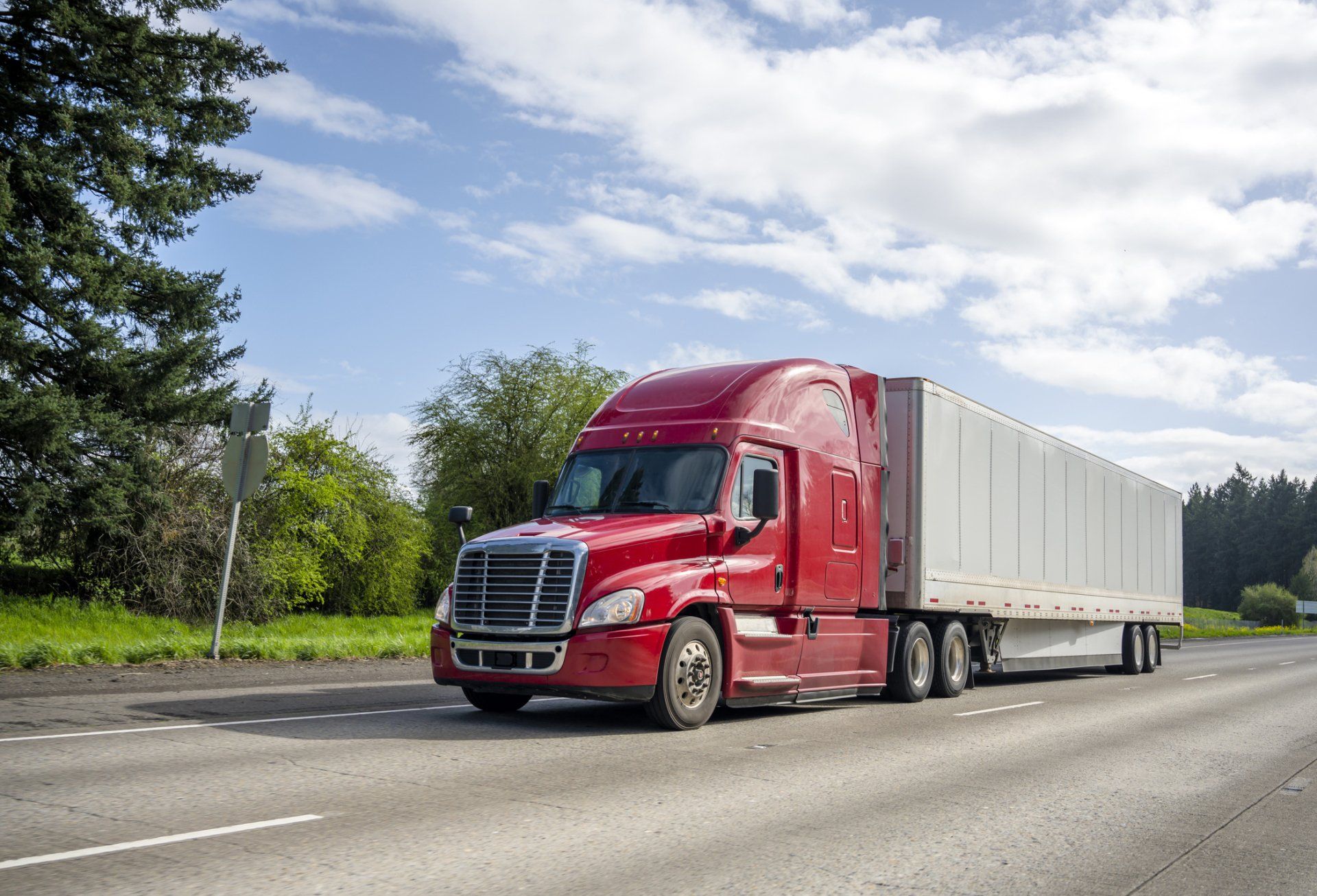 Red semi-truck hauling a white trailer on a road under a cloudy sky