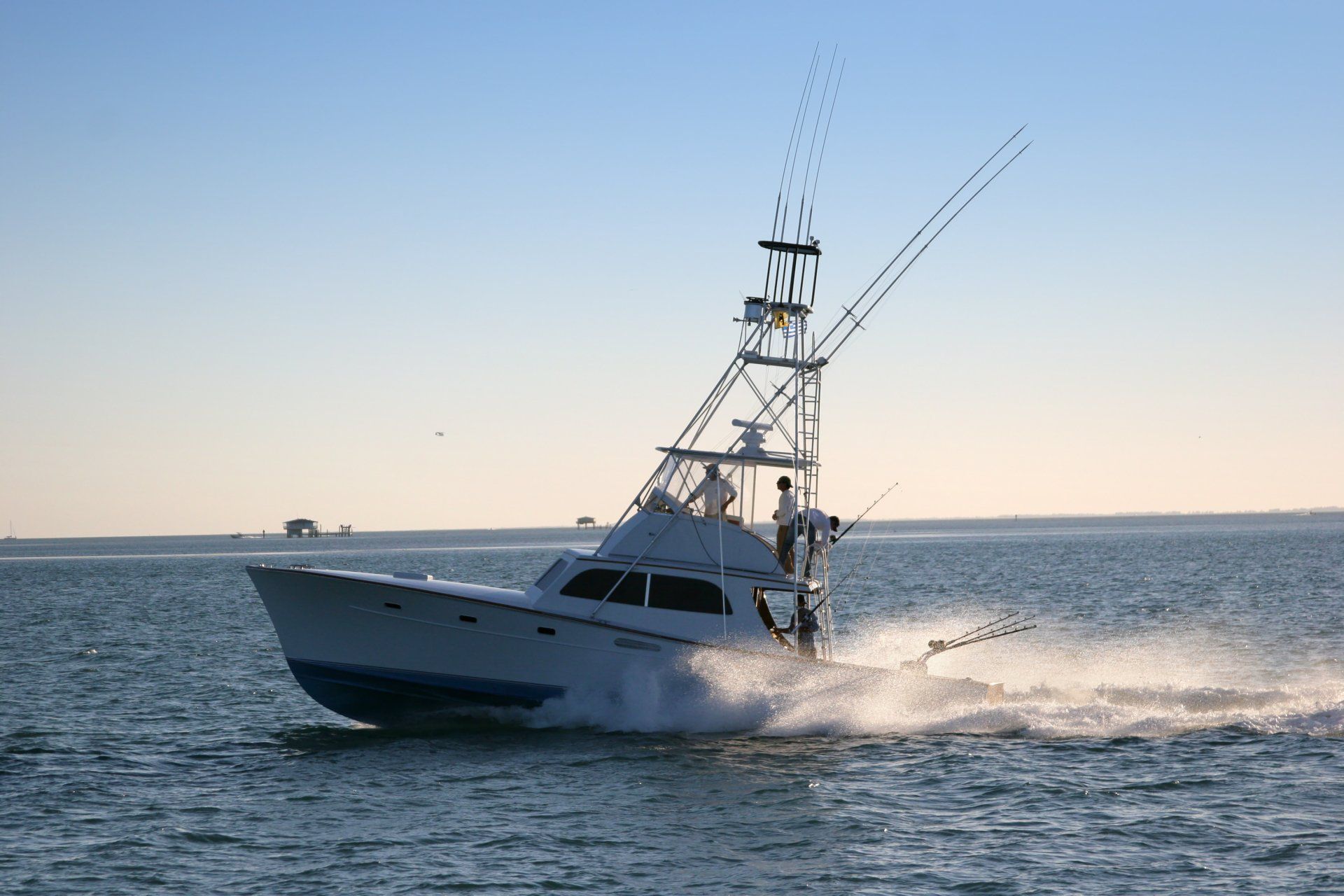 White sportfishing boat speeding across calm water at sunset, spraying wake under a clear sky