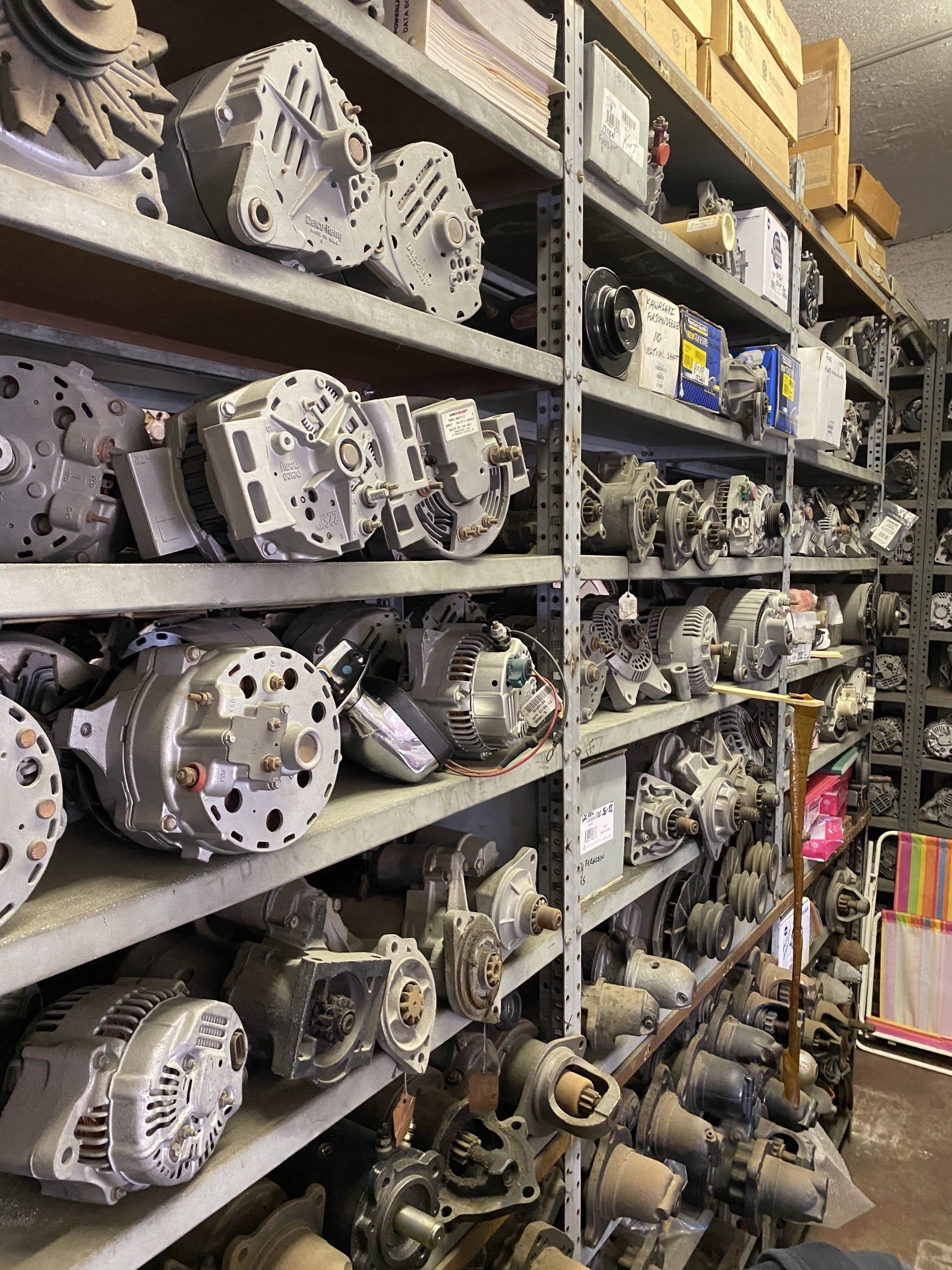 Shelves stacked with metal automotive parts and alternators in a warehouse aisle